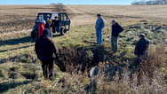 A group of people stand outside on near a field discussing how to handle existing tile