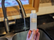 well water sampling bottle with sink and running faucet in background 