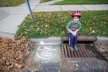 Child sitting next to a cleaned stormdrain with a pile of leaves nearby 