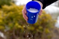 Hand holding a cup with salt, tilted and spreading salt on the ground 