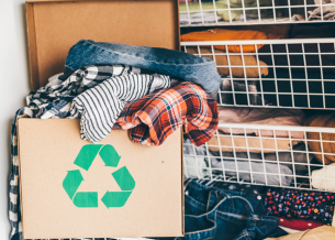 Box of with clothing spilling out of the top. Behind are wire baskets with clothing in them. 