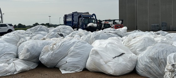 Large bags of plastic to be recycled with trucks and equipment in the background.