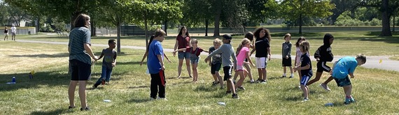 Students playing an outdoor game on a grassy field while learning about plant roots 