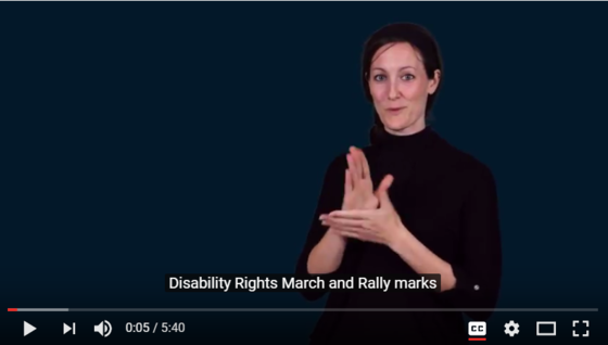 Still frame from the video about the Disability Rights March and Rally in celebration of the 27th anniverary of the ADA. Misty Schomberg is signing.