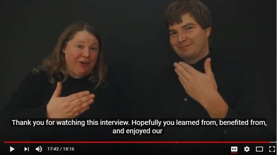 Freeze frame from the crash simulation video. Anne and Andrew are both signing, "thank you." The captioning is visible.