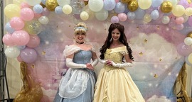 Two Disney princesses posing in front of a pastel balloon arch