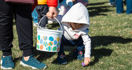 Young child picking up an easter egg while mother holds easter basket