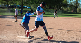 Guys playing softball, one guy crossing home plate while another tries to tag him out