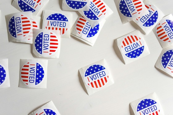 Scattered "I Voted" stickers with red, white and blue designs lie on a white surface, symbolizing voting and civic participation.
