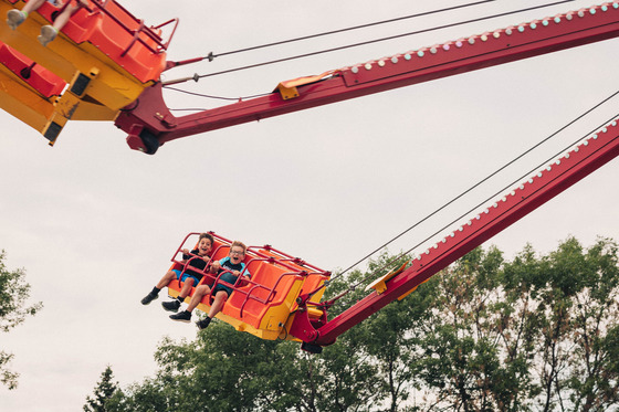 Children smile and shout as they ride a red and orange carnival swing ride above trees at Chanhassen’s Fourth of July Celebration.