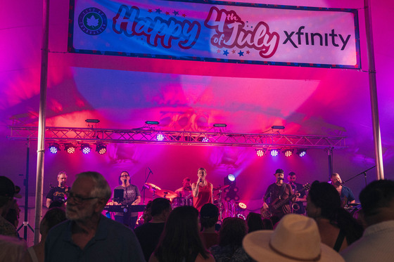 A crowd watches Good for Gary perform beneath a Happy 4th of July banner in the tent.
