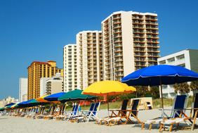 picture of a beach with chairs and umbrellas and behind, a bunch of multiunit living buildings