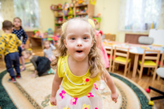 A little girl with down syndrome in a child care center smiles at the camera.