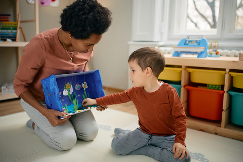 An African American teacher shows a diorama to a toddler.