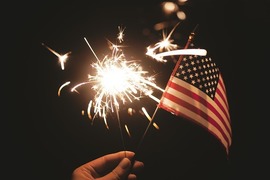 A hand holds a sparkler with an American flag