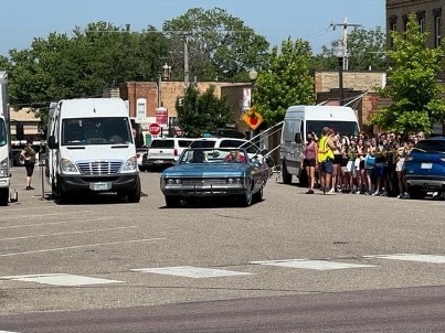Set of Marmalade. There is a cloud of people and a blue convertible.