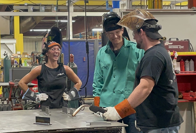 three smiling people standing at welding table