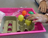 A woman's hand reaching into a half-carton of plastic, multi-colored eggs.