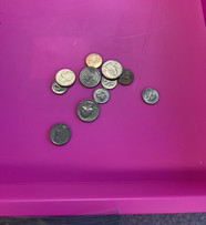 Various coins in a small pink plastic bin.