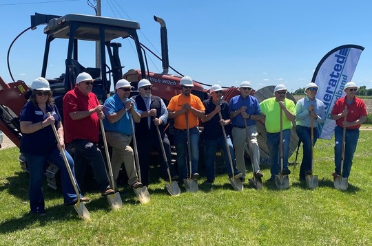 10 ceremony attendees pose in front of a large tractor, holding shovels. 