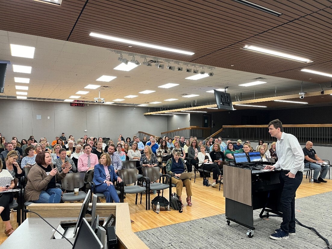 Man standing behind a podium addresses a room of people.