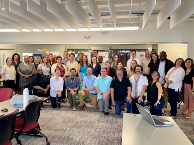 A large group of people stand posing for a picture in an office space.