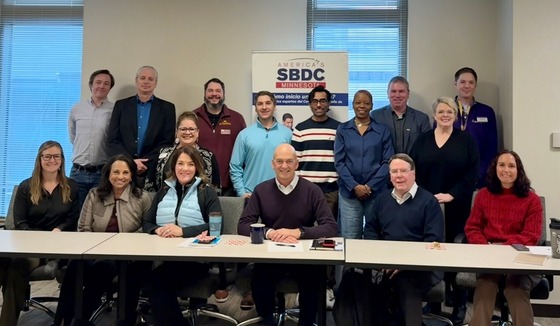 15 people stand in front of a sign for the Small business Development Center