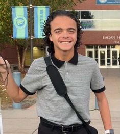 Preston standing with a cane in his hand. He is wearing a grey and black polo with black pants.