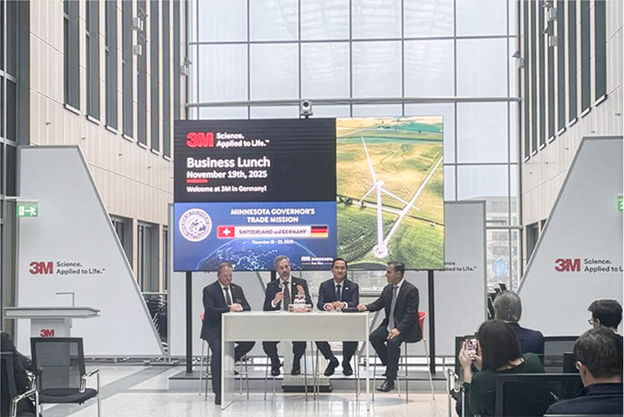 Commissioner Varilek sits at a table with three other people, speaking in front of an audience.