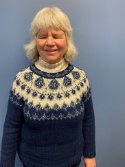 Allison smiling standing in front of a blue wall wearing a blue and white turtleneck sweater. 