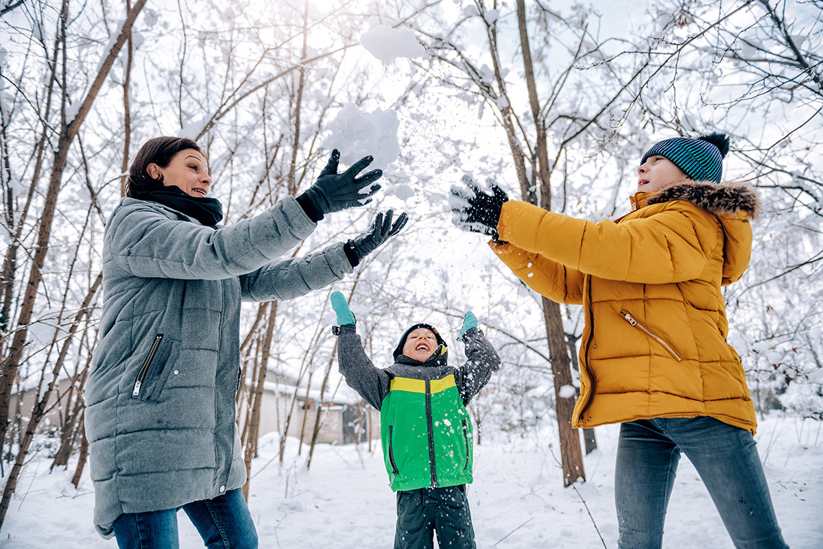 Mother and two children tossing snow in the air in a forest.
