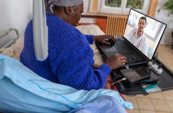 woman in bed communicating with doctor on computer screen
