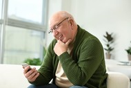 older adult smiling as holds his cell phone