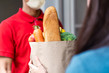 man in face covering delivering bag of groceries to woman