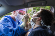 person in car getting swabbed by person in medical scrubs standing outside