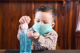 Child in mask using hand sanitizer