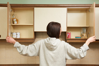 woman opening cupboard doors and seeing very little food on her shelves