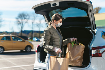 woman loading two bags of groceries into a trunk