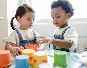 two toddlers playing with plastic cubs at a little table