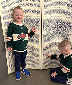 two boys in front of a large poster of hundreds of names of adopted children