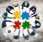 People seated around a table putting together four giant brightly colored puzzle pieces.