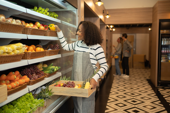 A woman stocking fruits and vegetables in a store cooler.