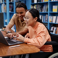 Woman with a disability working on a laptop with help from another person