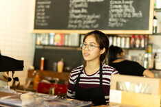 Teen waitress wearing an apron standing in a coffee shop.