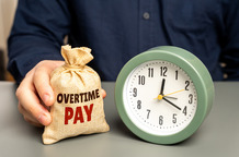 A man holds a money bag with overtime pay near a clock.