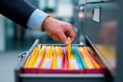 A hand is seen reaching for color-coded files in a cabinet drawer