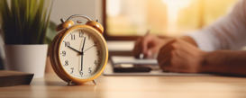 Alarm clock on table near business person working on laptop