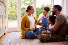 Army Family With Pregnant Mother Sitting On Floor In Lounge At Home.