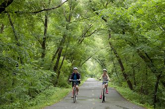 two children on bikes on a paved trail in the woods