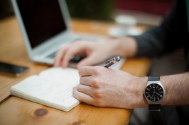 A photo of a man writing notes next to a computer